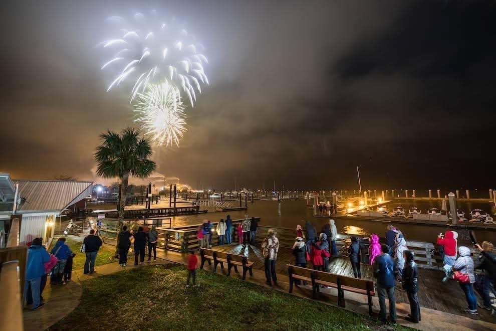 Families on blankets along the Fernandina Beach pier watching fireworks at dusk.
